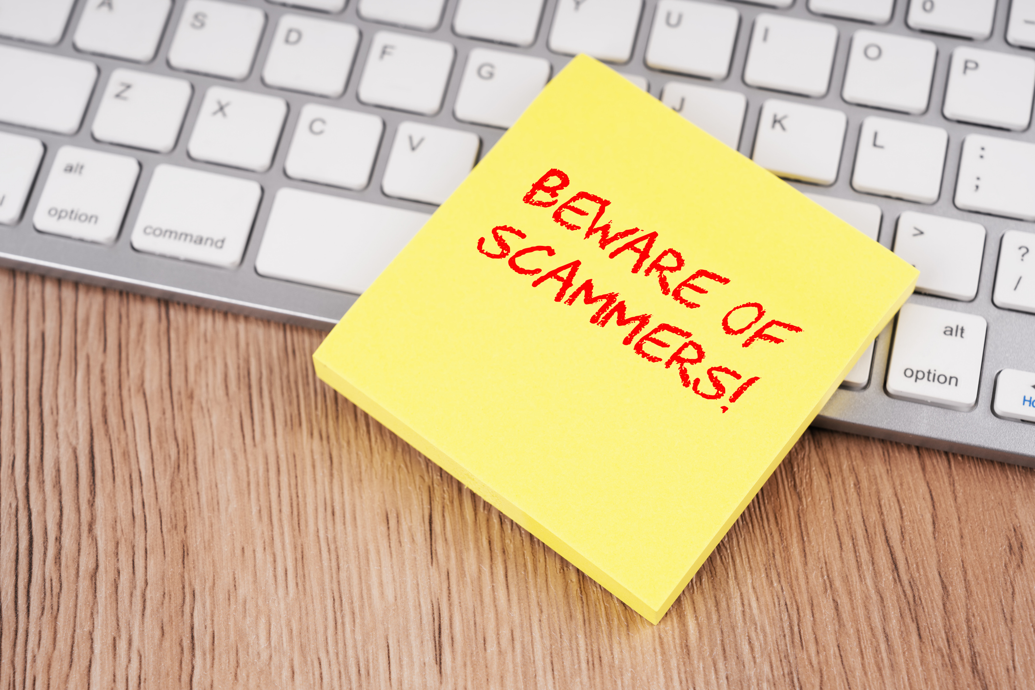 Post it note reading "Beware of Scammers!" on a computer keyboard. 