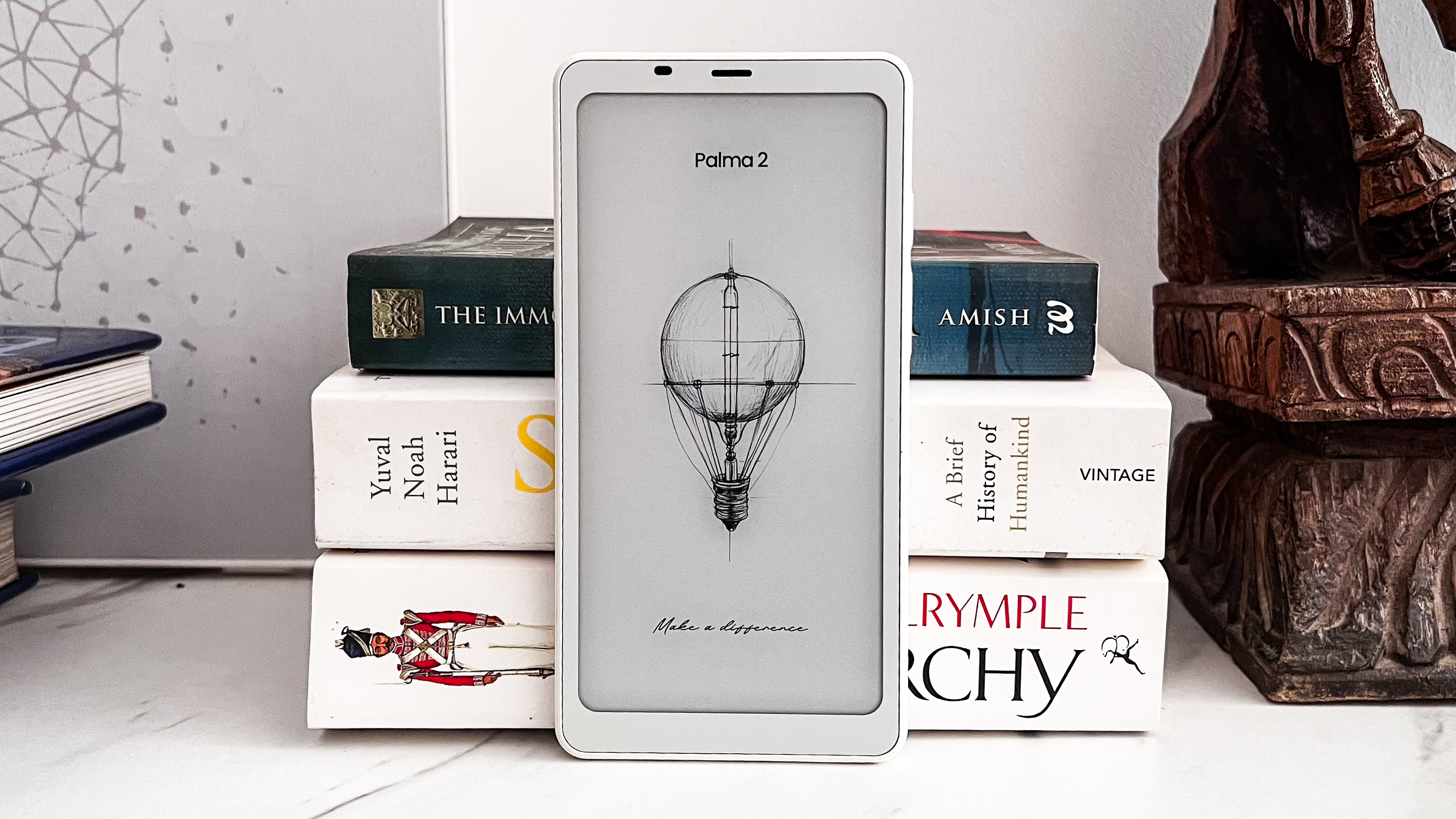 The Onyx Boox Palma 2 standing upright against a pile of books on a table