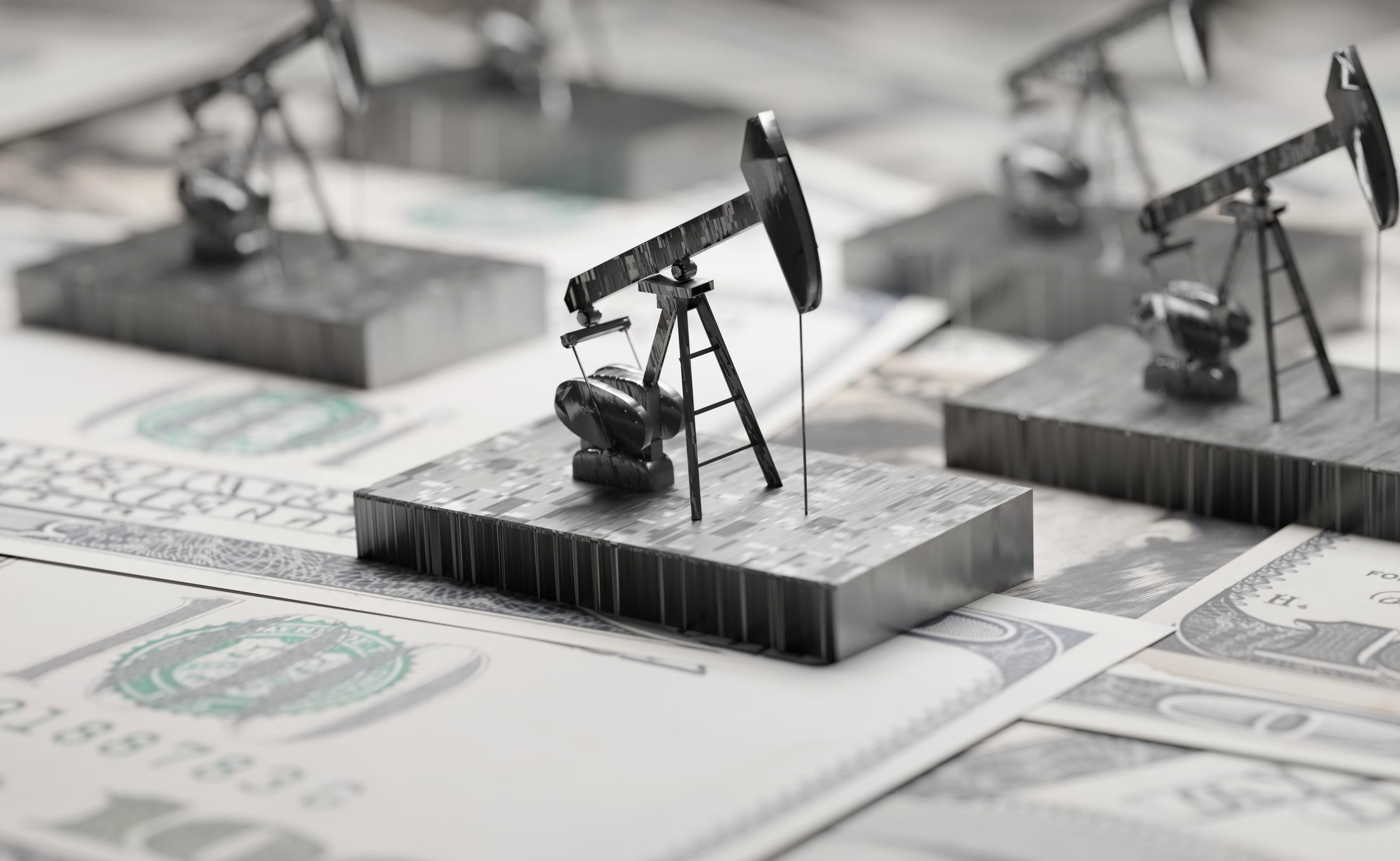 several small models of oil drills sitting on top of one-hundred dollar bills