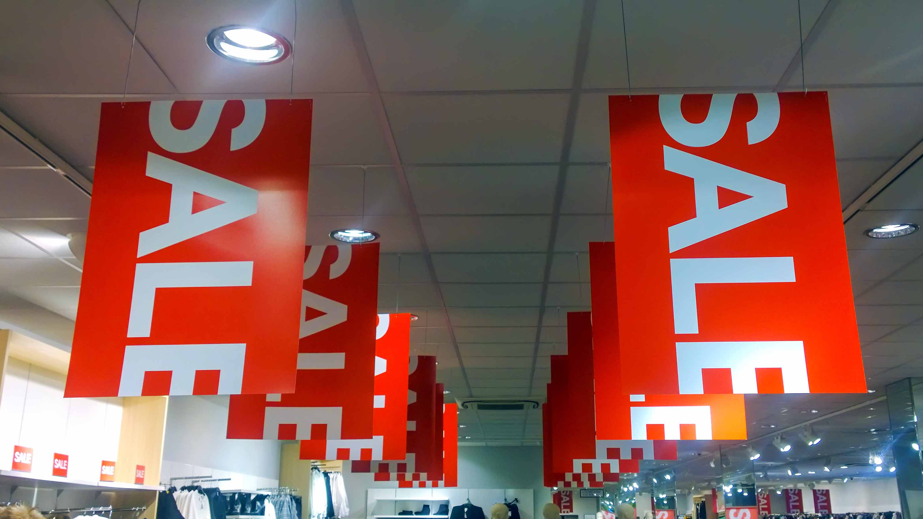 red sign with white "sale" letters hanging from store ceiling