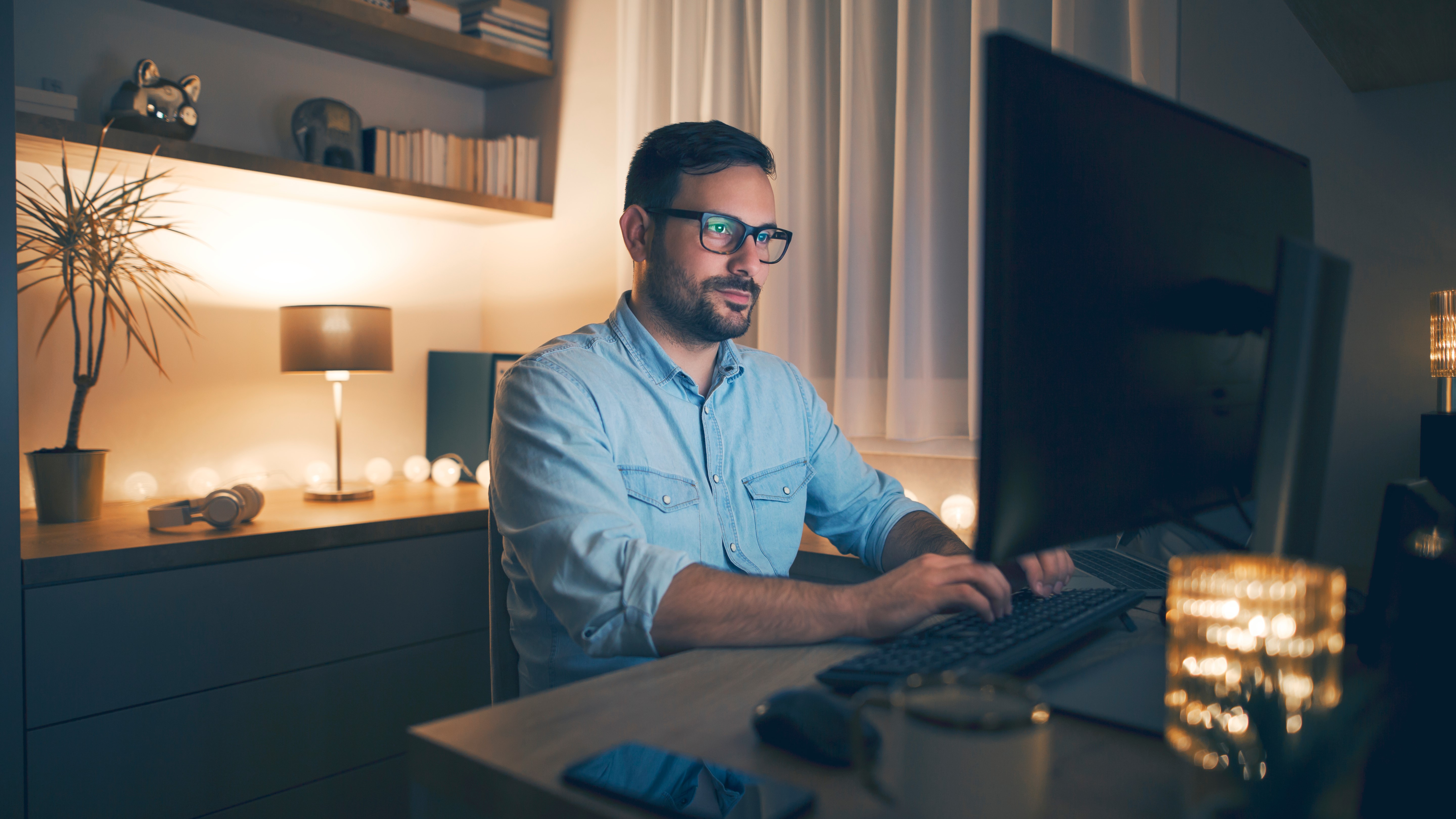 A man sitting at his desk in the evening and using a desktop computer