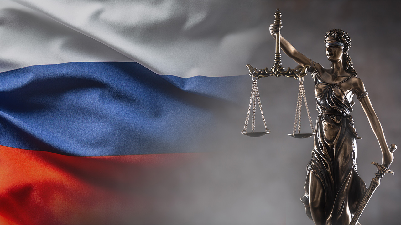 Bronze legal stature holding scales, with Russian flag behind it