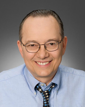 David Crook smiles against a grey background.