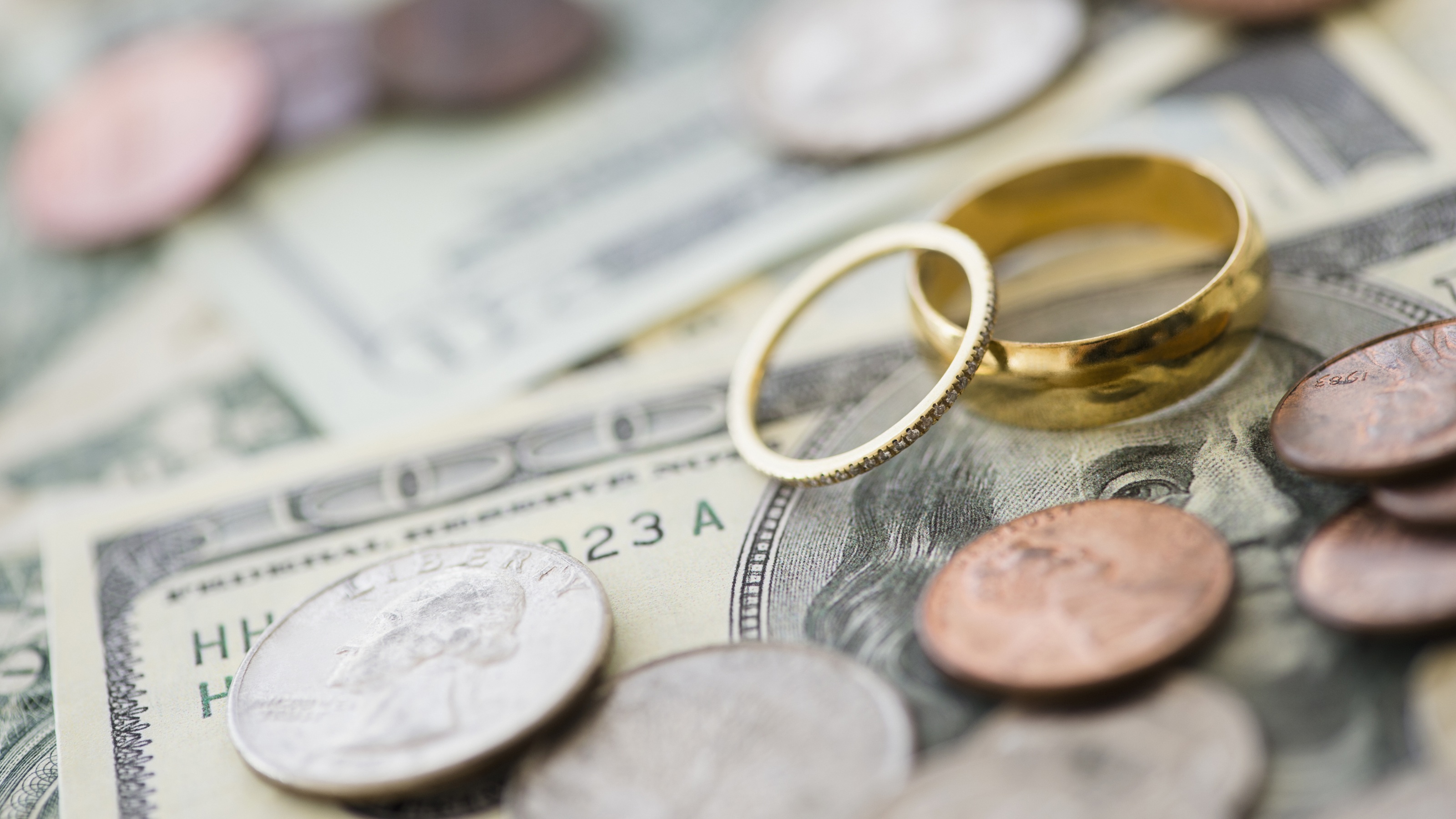 Coins scattered around wedding rings sitting on top of cash.