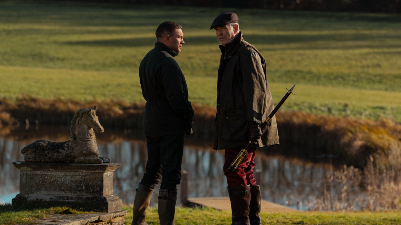 Tom Hardy and Pierce Brosnan covertly chat by a lake in MobLand