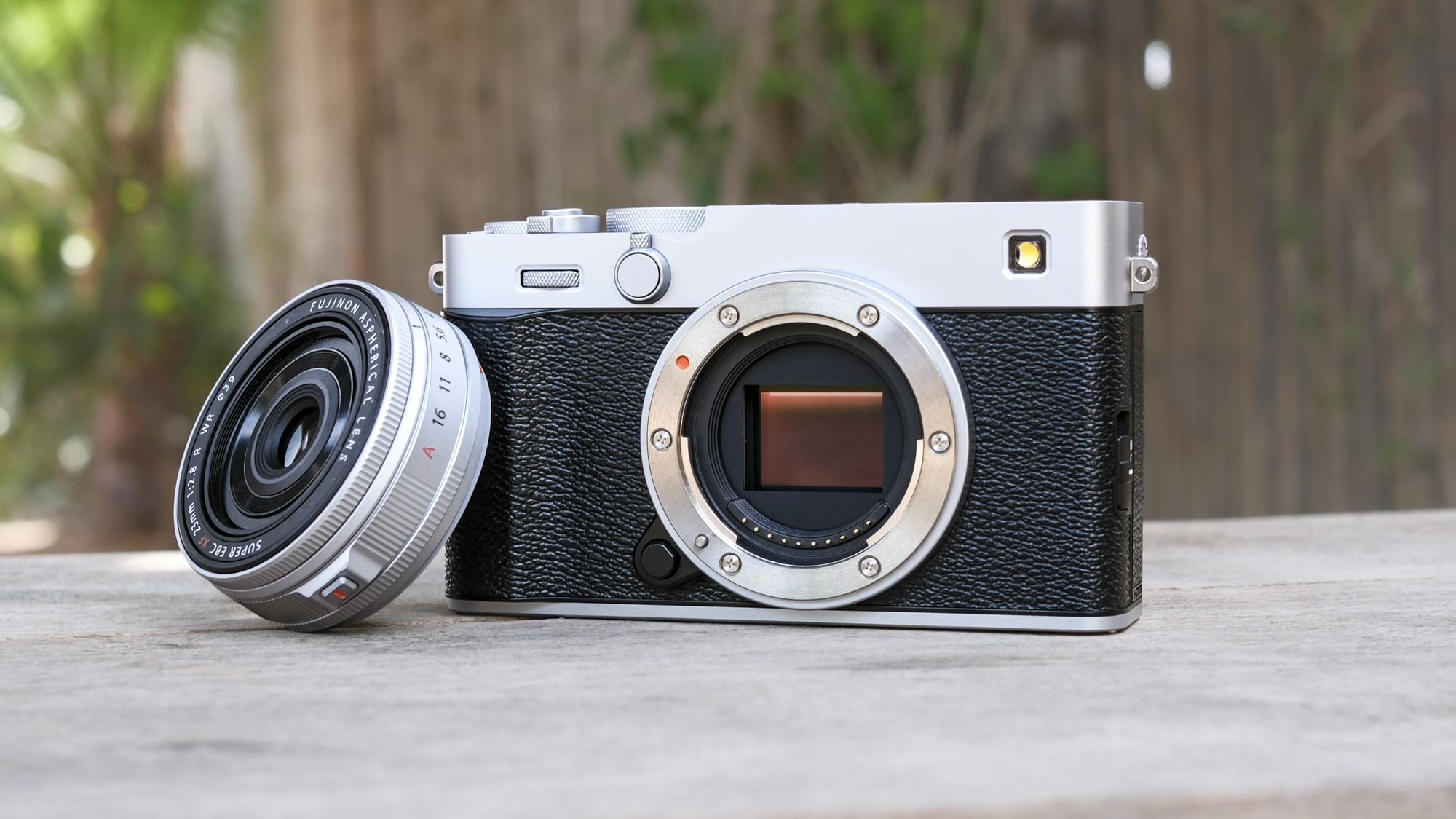 Fujifilm X-E5 on a wooden bench, with the XF 23mm f/2.8 lens removed and propped up against the camera