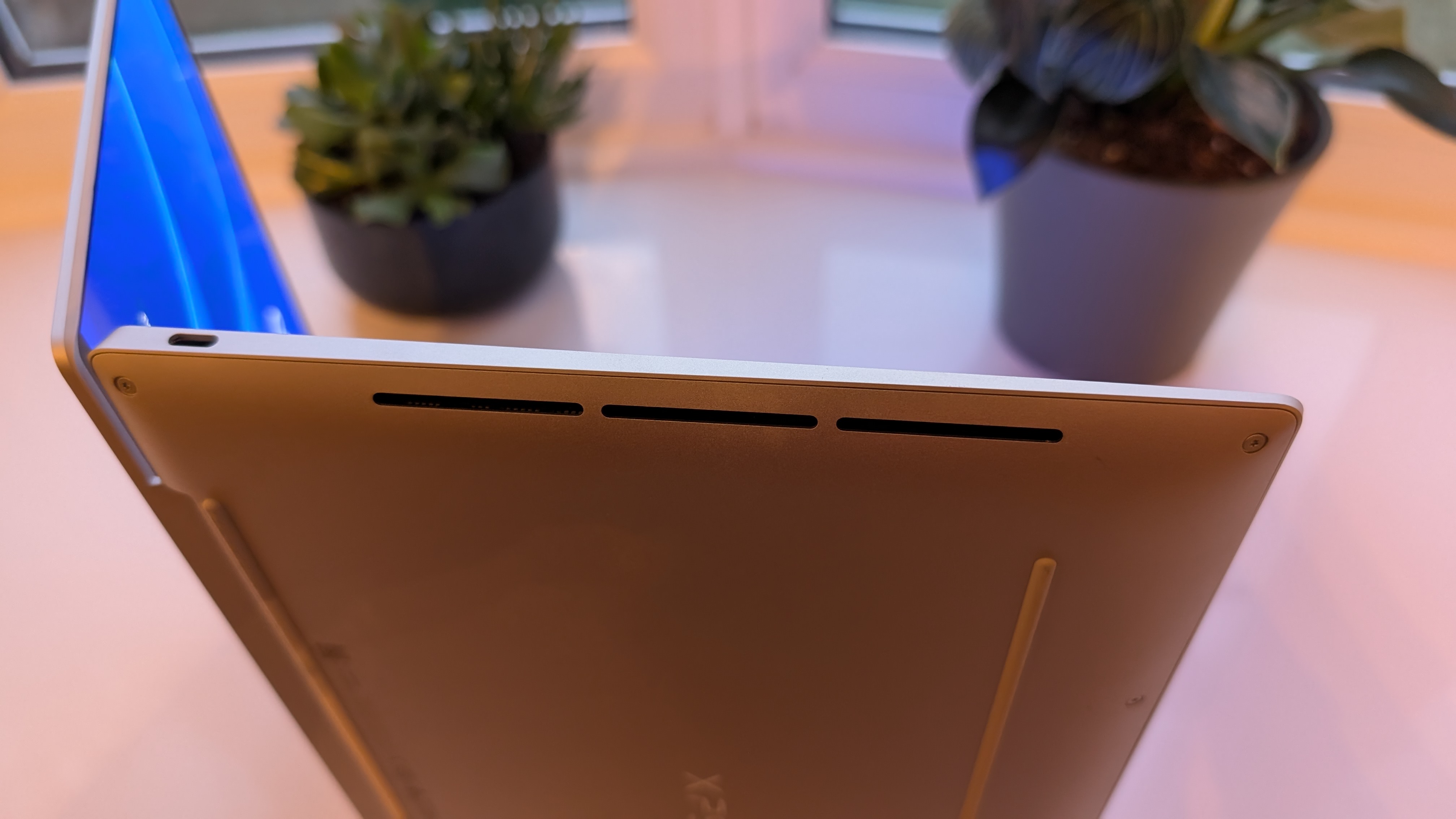 The Dell XPS 13 pictured on a white surface in front of a window with two potted plants.